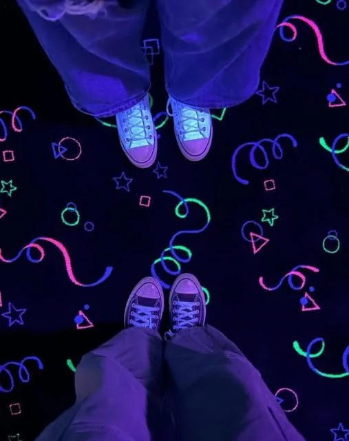 Two pairs of shoes stand together on a colorful glow-painted floor at Southern Lanes